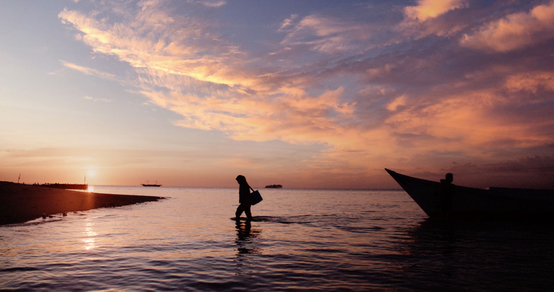 Rahmi (Mimi), a midwife, carries a cold box filled with vaccines at sunset after disembarking from a boat on Pala Island, Indonesia.